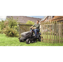 Un homme conduit un tracteur de pelouse sur une pelouse à côté d'une clôture en bois.