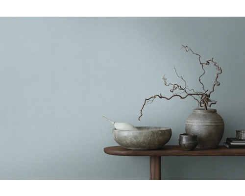 Bol décoratif, vase et branches sur une table en bois devant un mur