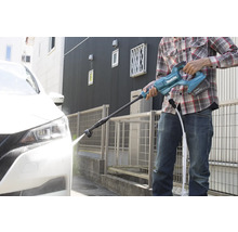 Eine Person reinigt mit einem Akku-Hochdruckreiniger ein Auto vor einem Haus.