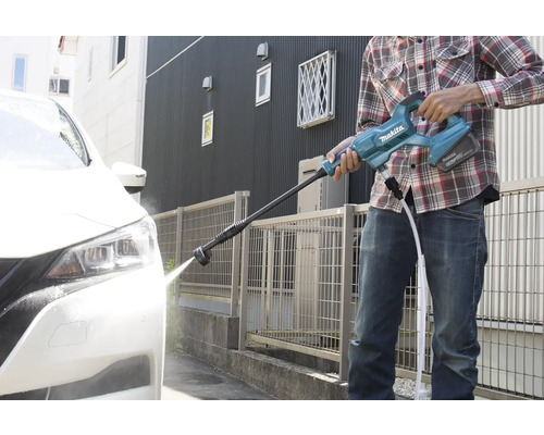 Eine Person reinigt mit einem Akku-Hochdruckreiniger ein Auto vor einem Haus.