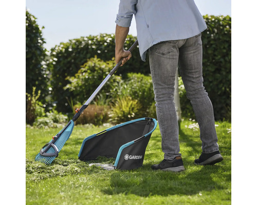 Scène de jardin avec un jardinier ratissant la pelouse avec un râteau à feuilles et un collecteur de gazon de Gardena