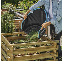 Une personne vide un sac à feuilles Gardena dans un bac à charbon de bois en bois dans le jardin.
