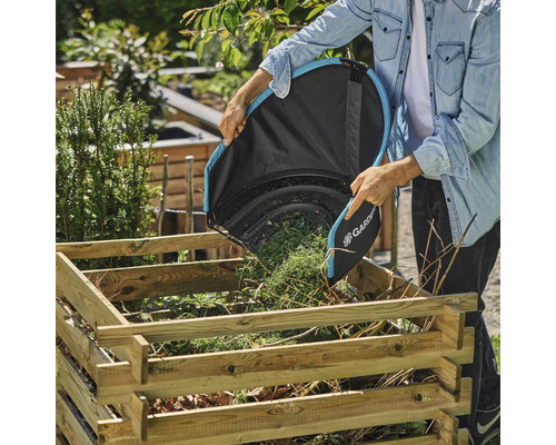 Une personne vide un sac à feuilles Gardena dans un bac à charbon de bois en bois dans le jardin.