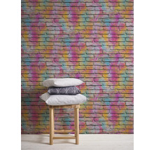Mur avec un papier peint en briques colorées et une pile de coussins sur un tabouret.
