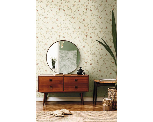 Wohnzimmer mit Blumentapete, Kommode, Spiegel und Dekorationen.