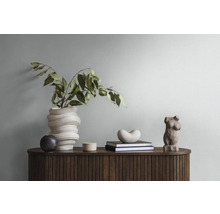 Arrangement décoratif sur un buffet avec façade rainurée, comprenant une sculpture abstraite, un vase avec des branches et des livres