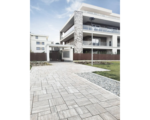 Photo extérieure d'un immeuble d'habitation moderne avec allée pavée et éléments décoratifs.