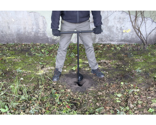 Une personne utilise une tarière pour percer un trou dans le sol.