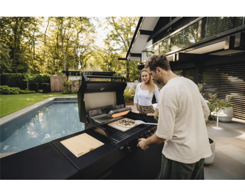 Un homme et une femme préparent une pizza sur un grill extérieur à côté d'une piscine