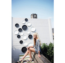 Wanddekoration mit Tellern in einem Aussenbereich mit einer Frau auf einer Bank