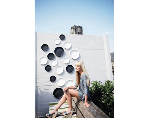 Wanddekoration mit Tellern in einem Aussenbereich mit einer Frau auf einer Bank