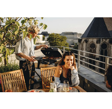 Personen grillieren auf einer Dachterrasse mit Grill und Gartenmöbeln.