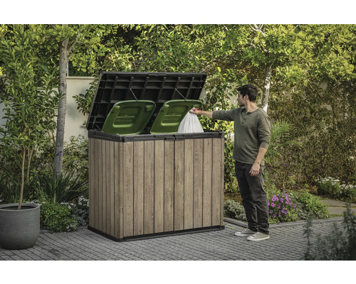 Cache-poubelle en bois avec deux poubelles vertes et une personne jetant un sac poubelle à l'intérieur