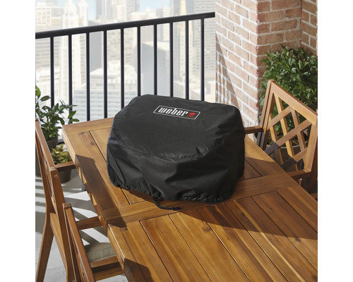 Housse de protection noire pour barbecue Weber sur une table en bois