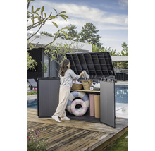 Une femme range une boîte de jardin grise contenant des accessoires de piscine sur une terrasse en bois.