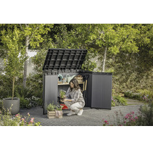 Scène de jardin avec armoire à outils ouverte dans laquelle une femme range des ustensiles de jardin.