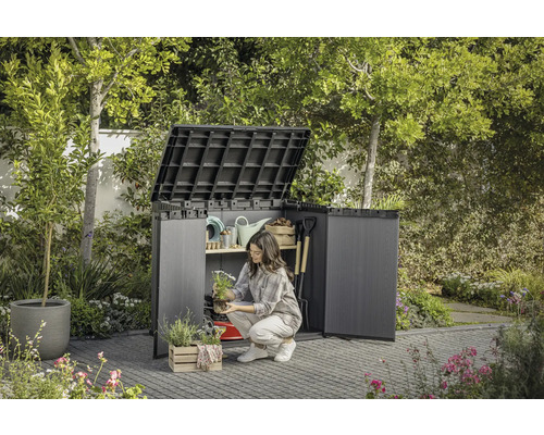 Scène de jardin avec armoire à outils ouverte dans laquelle une femme range des ustensiles de jardin.