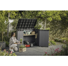 Une femme plante des fleurs devant un abri de jardin ouvert avec des outils de jardinage