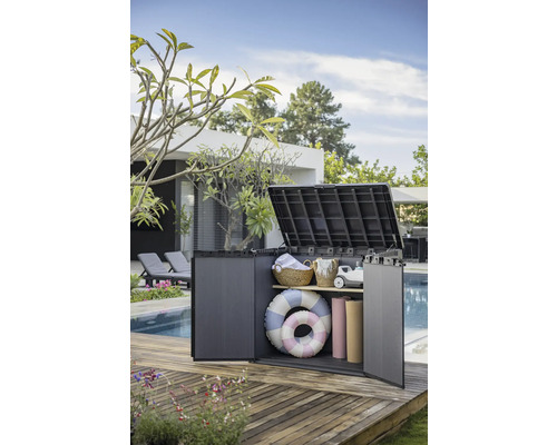 Geöffnete Gartenbox aus Kunststoff auf einer Holzterrasse, gefüllt mit Gartenzubehör