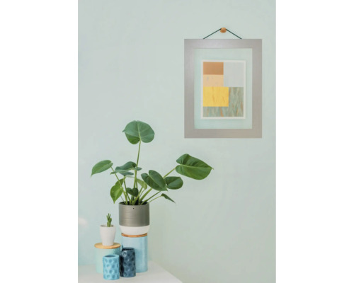 Dekoratives Stillleben mit Zimmerpflanze, Keramikgefäßen und gerahmtem Bild an der Wand.