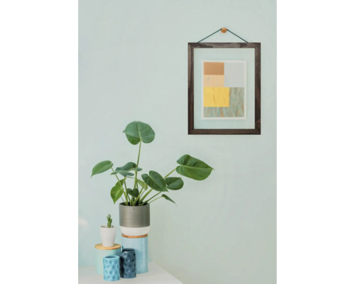 Dekoratives Interieur mit Zimmerpflanze, Bild und kleinen Gefäßen auf einem Tisch.