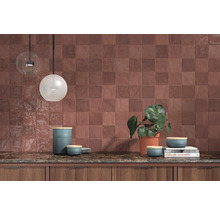 Scène de cuisine avec des carreaux muraux carrés, un plan de travail et des éléments décoratifs tels que des luminaires et une plante.