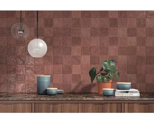 Scène de cuisine avec des carreaux muraux carrés, un plan de travail et des éléments décoratifs tels que des luminaires et une plante.