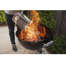 Une personne verse du charbon de bois incandescent d'une cheminée d'allumage dans un barbecue sphérique.