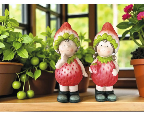 Zwei dekorative Erdbeerfiguren zwischen Pflanzen auf einem Regal
