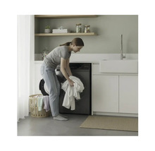 Femme charge un lave-linge dans une buanderie avec des étagères et un lavabo