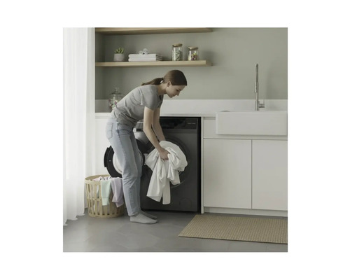 Femme charge un lave-linge dans une buanderie avec des étagères et un lavabo