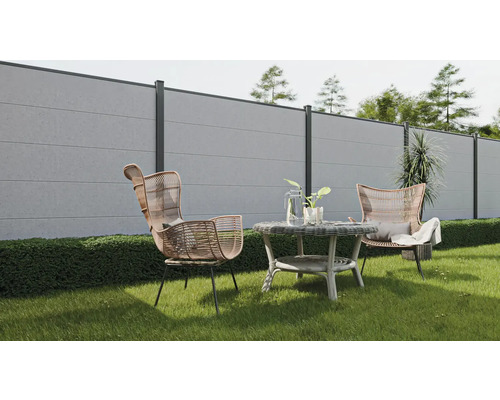 Gartenszene mit Betonzaun, zwei Rattansesseln und einem runden Tisch auf einer Rasenfläche.