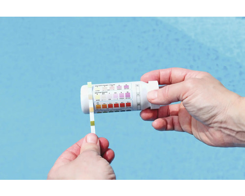 Une personne teste l'eau de la piscine avec une bandelette et un kit de test.