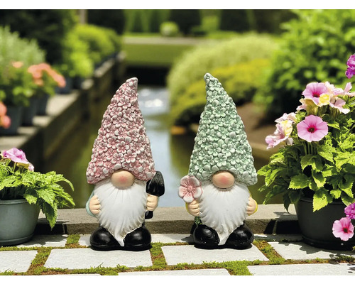 Zwei Gartenzwerge mit blumengeschmückten Hüten und Gartenwerkzeug auf einer Steinmauer