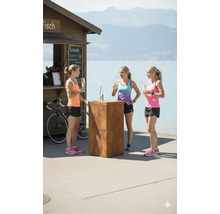 Drei Frauen stehen an einem Stehtisch aus Metall vor einem Kiosk und dem Ufer eines Sees.