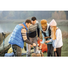 Groupe d'amis en camping préparant de la nourriture au-dessus du feu de camp, avec une tente en arrière-plan.