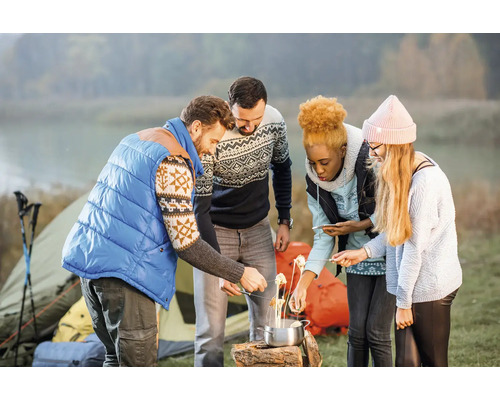 Groupe d'amis en camping préparant de la nourriture au-dessus du feu de camp, avec une tente en arrière-plan.