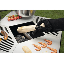 Table de barbecue avec des aliments et une personne ajoutant du bois