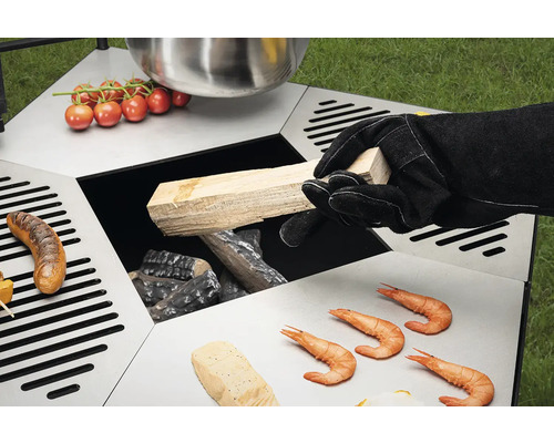 Table de barbecue avec des aliments et une personne ajoutant du bois