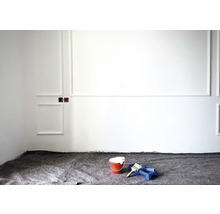Travaux de rénovation avec seau de peinture, pinceau et rouleau devant un mur blanc avec des éléments de stuc