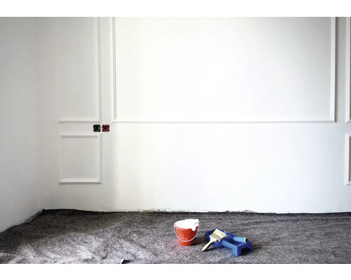 Pièce avec outils de peintre, seau de peinture, pinceau et bac à peinture devant un mur blanc avec moulures décoratives