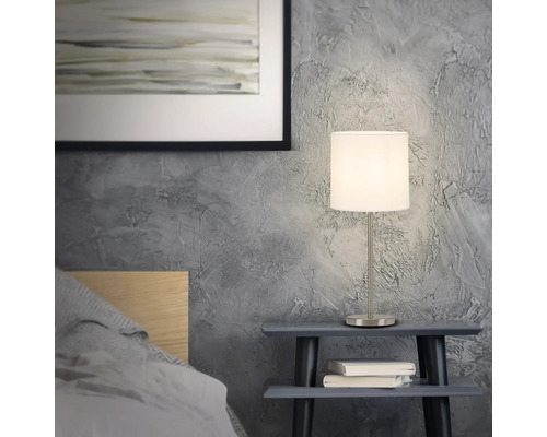 Nachttischszene mit einer Tischlampe auf einem kleinen Tisch neben einem Bett