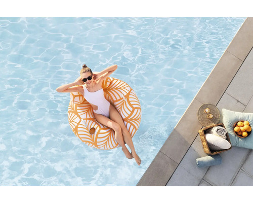 Femme se détend sur une bouée dans la piscine, avec des serviettes et des boissons au bord de la piscine