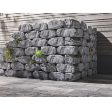 Pierres de jardin grises empilées avec plantations devant un mur en bois