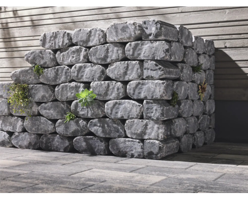 Pierres de jardin grises empilées avec plantations devant un mur en bois