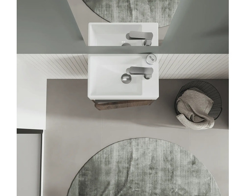 Vue de dessus d'une salle de bains avec lavabo, robinet, miroir, tapis rond et panier à linge