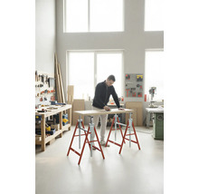 Un homme ponce une planche de bois sur des tréteaux dans un atelier