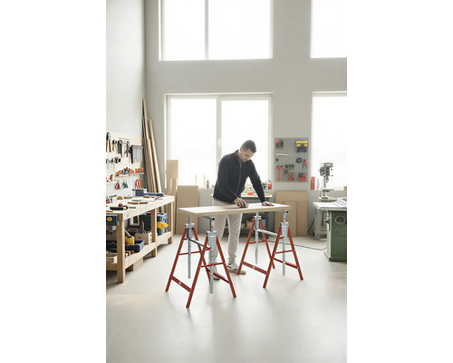 Un homme ponce une planche de bois sur des tréteaux dans un atelier