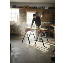Homme ponçant une planche de bois sur deux tréteaux dans un atelier.
