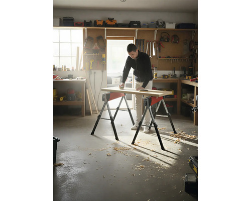 Homme ponçant une planche de bois sur deux tréteaux dans un atelier.